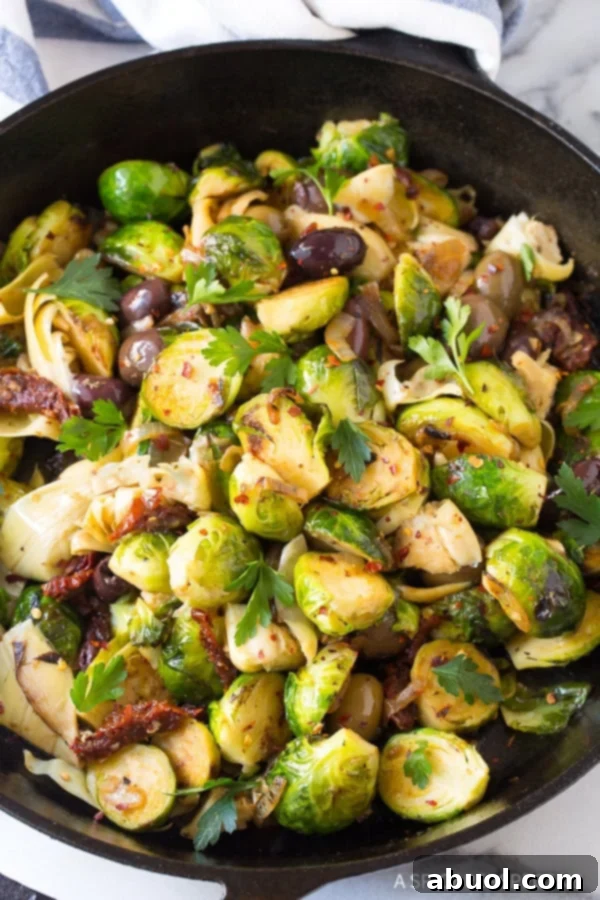 Braised brussels sprouts with sun-dried tomatoes, greek olives, artichoke hearts and fresh chopped parsley in a cast iron skillet.