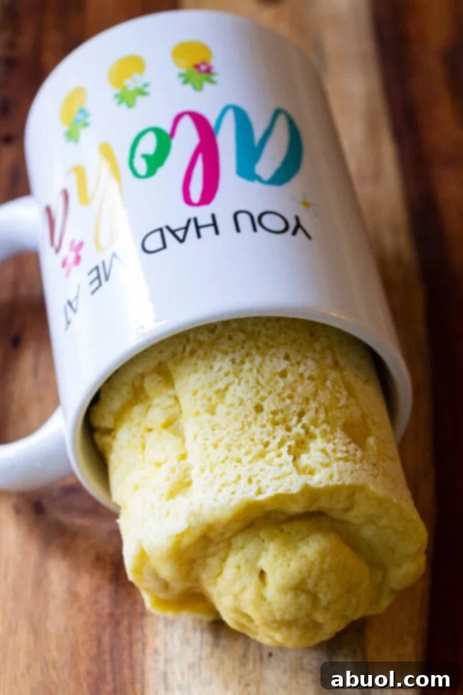 A white mug lying on its side, with a perfectly baked, fluffy loaf of low-carb microwave bread half-emerging from it.