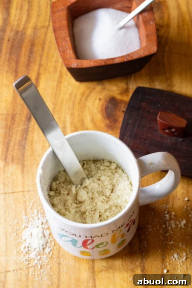 Inside a white mug, fine almond flour is being mixed smoothly with a metal spoon, creating the batter for the low-carb bread.