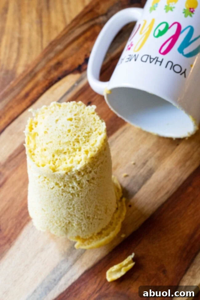 A freshly baked loaf of magic mug bread rests on a wooden cutting board, positioned next to the now empty white mug, ready to be sliced and enjoyed.