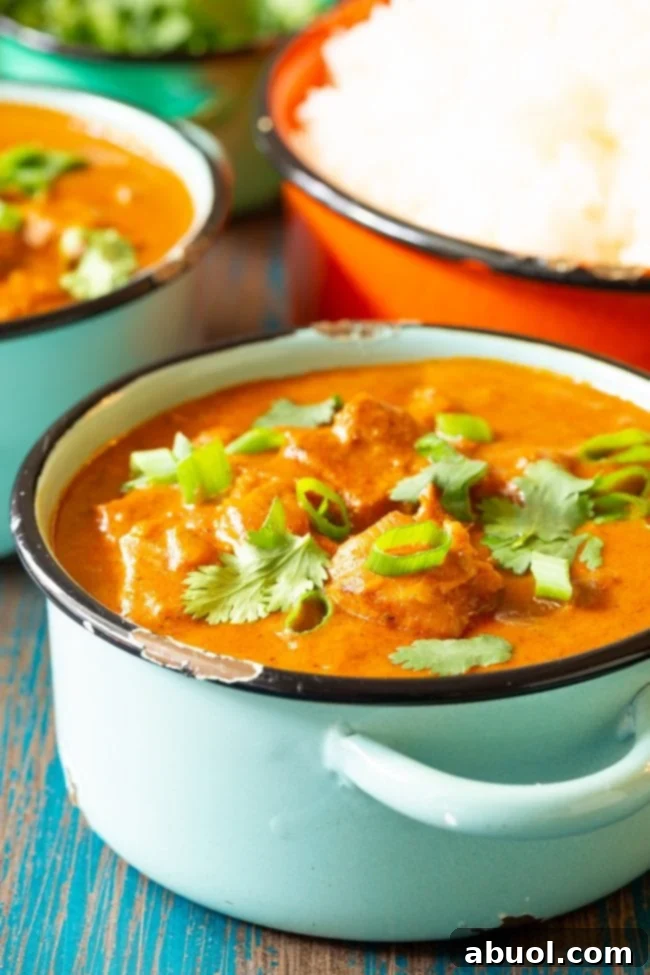 Small bowl of Indian butter chicken topped off with cilantro and scallions, close up.