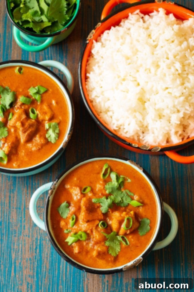 Overhead of two bowls of butter chicken with a large bowl of rice on the side, ready for family dinner.
