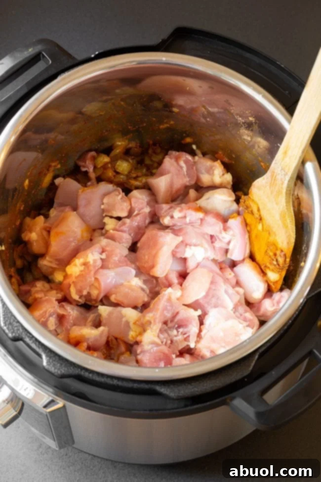 Cubed chicken thighs topped with spices in an instant pot cooker.