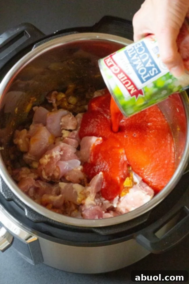 Tomato sauce being poured over uncooked chicken.