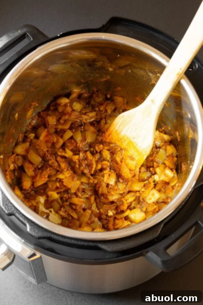 Wooden spoon mixing chicken in pressure cooker.