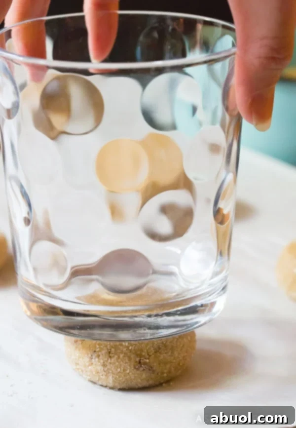 Caramelized Butter Delights 8 A drinking glass pressing down cookie dough balls to flatten them before baking.