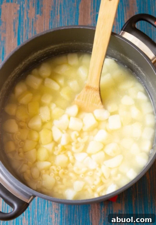 Pasta and potatoes boiling in a pot with a wooden spoon.