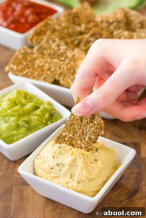 Hand dipping a cracker into a white square bowl of hummus.