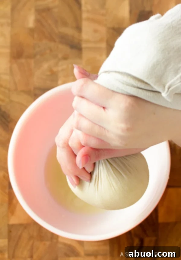 Hands squeezing water from a cheesecloth bundle filled with steamed cauliflower.