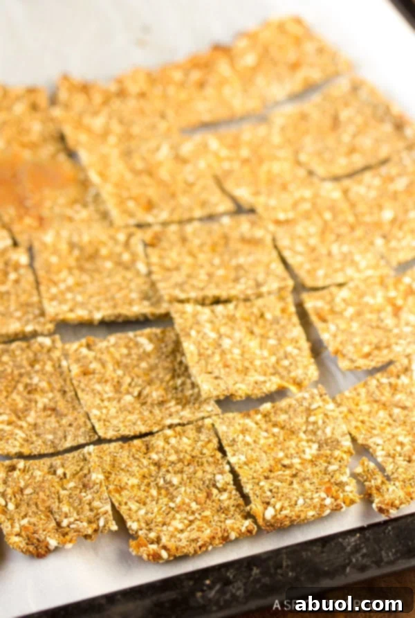 A parchment paper lined baking sheet covered with squares of grain free cauliflower crackers.