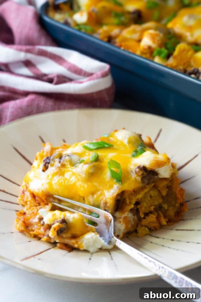 A piece of Doritos casserole on a plate with a bite taken out by a fork, showing its delicious layers.