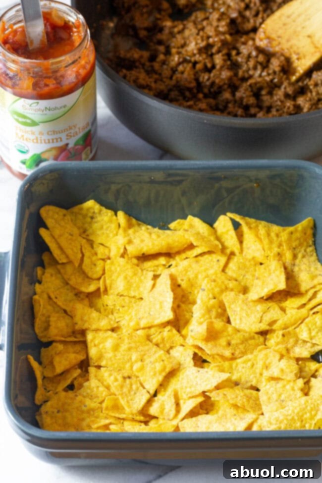 Crushed Doritos forming the base layer in a baking tray.