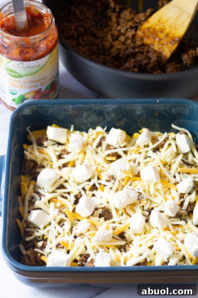 Doritos and minced meat topped with shredded cheese and cream cheese cubes in baking dish.