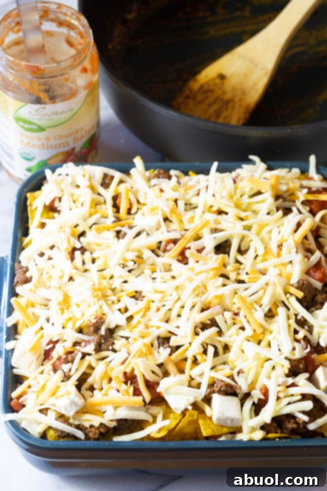 Baking dish with Dorito mixture, meat, and salsa topped off with the final shredded cheese layer.