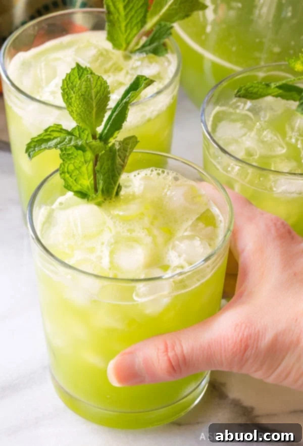 Three glasses of cucumber agua fresca with a hand grabbing one glass. 