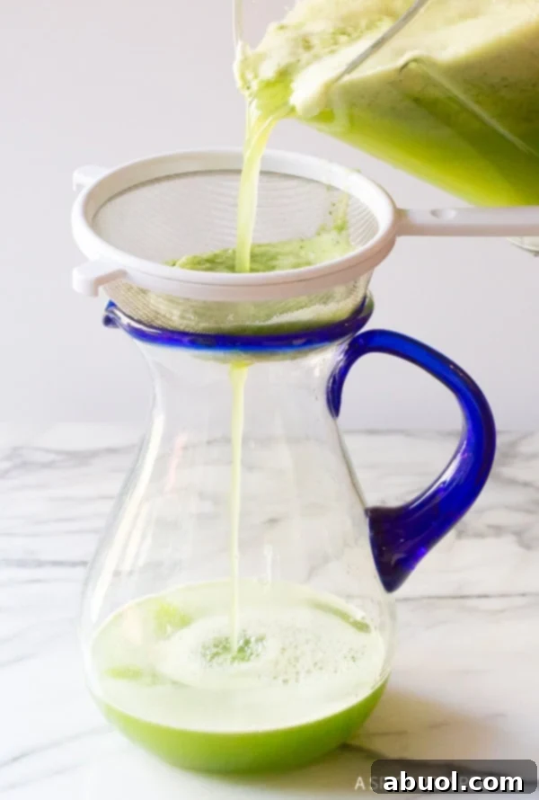 Hand pouring the agua fresca from the blender into a pitcher with a strainer on top. 