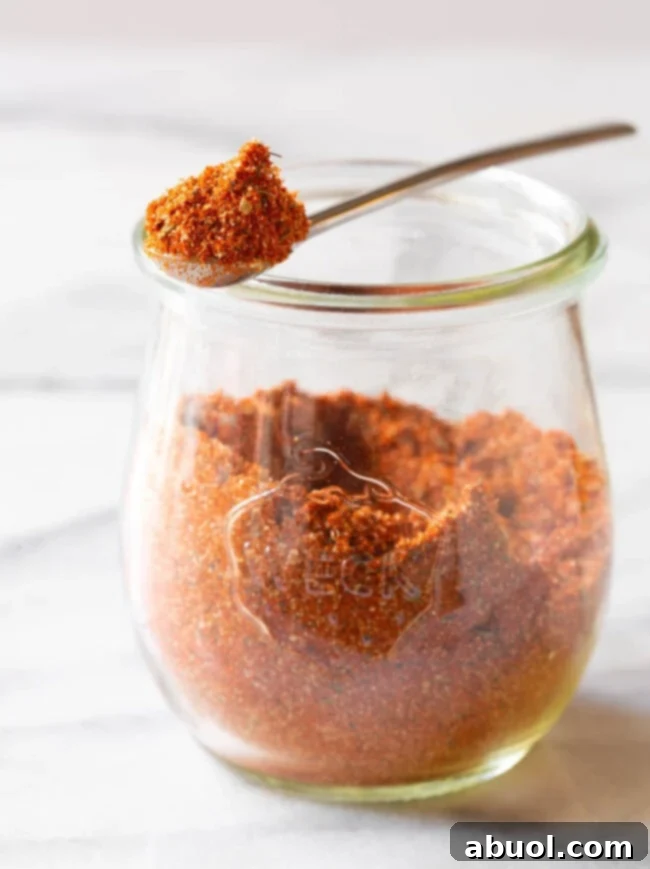 A glass jar filled with homemade blackened seasoning, with a metal spoon holding a spoonful of the seasoning mixture over the jar.