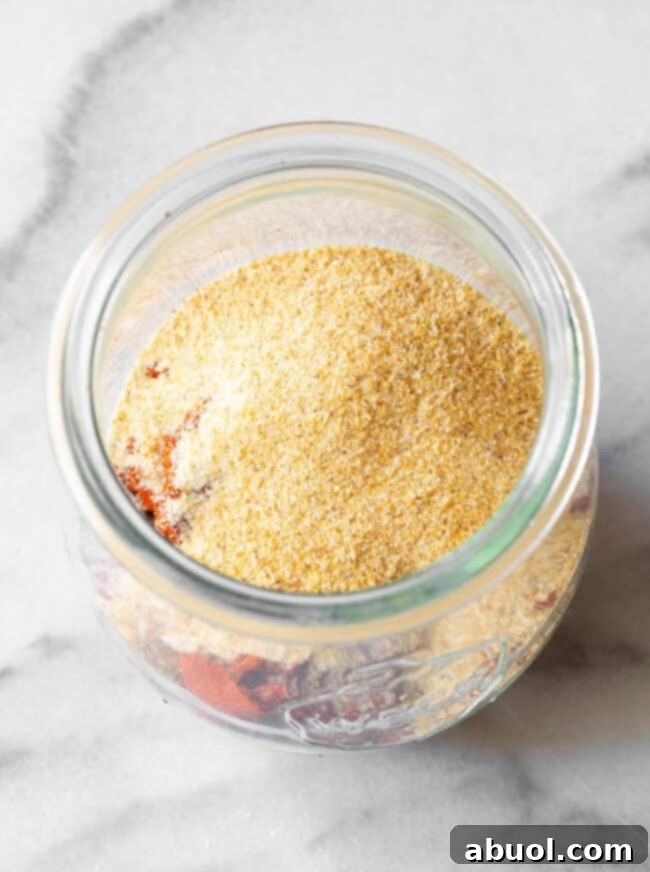 An overhead view of a clear glass jar brimming with richly colored homemade blackened seasoning.