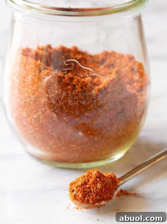 A glass jar full of homemade blackened seasoning, with a metal spoon resting in the foreground holding a spoonful of the seasoning.
