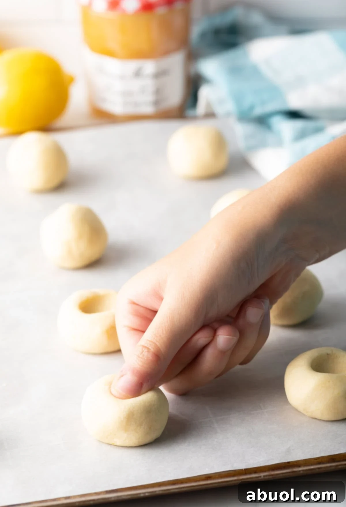 Sheet pan displaying lemon thumbprint cookie dough balls with freshly pressed indents, ready for their lemon custard filling.