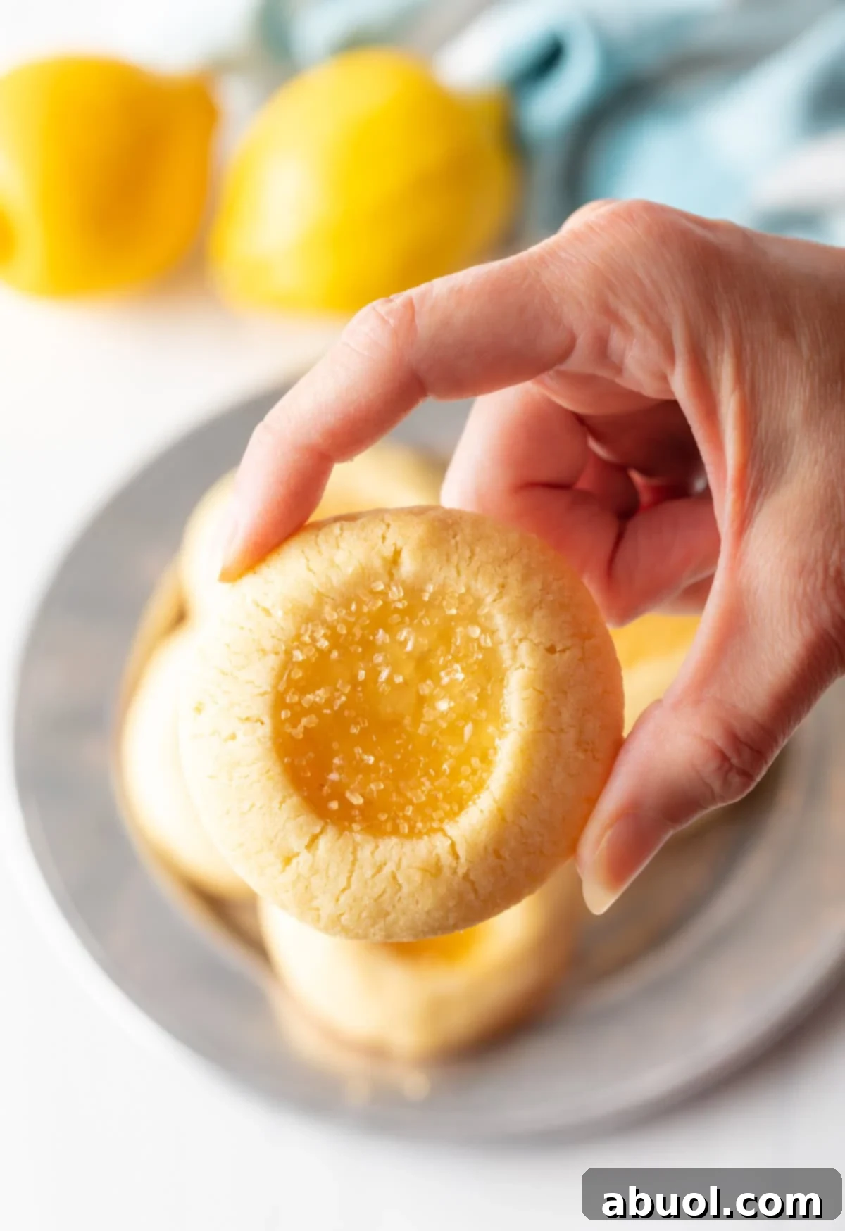 A hand gently holds up a lemon drop cookie, showcasing its golden crust, delicate lemon center, and inviting texture.