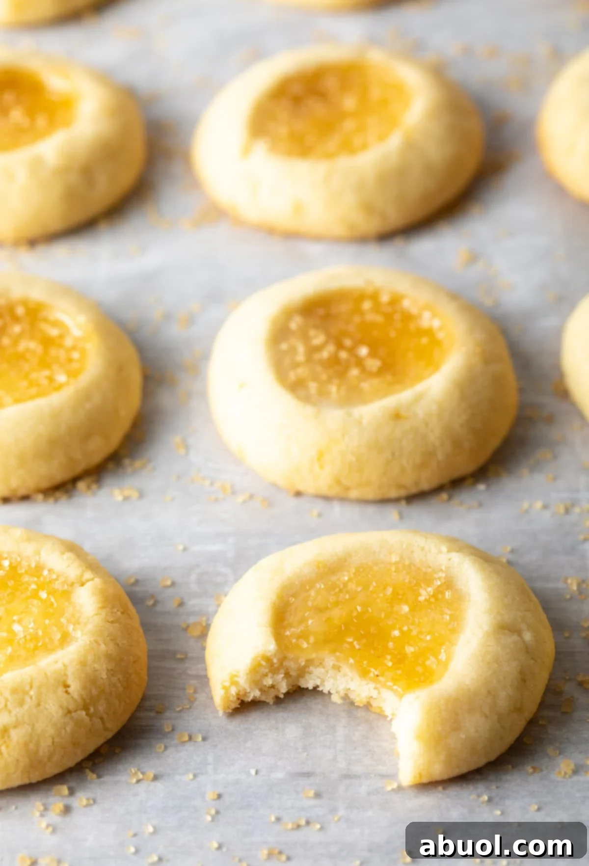 A single lemon thumbprint cookie with a bite taken out, resting on a baking sheet with other cookies, inviting a taste.