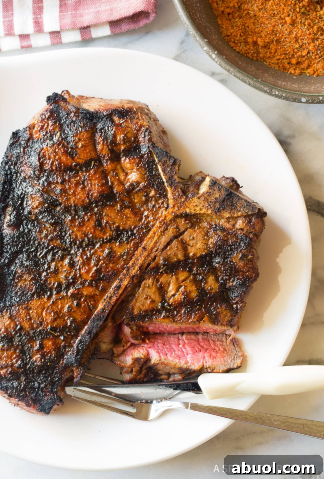 Overhead shot of a perfectly cooked steak on a white plate with fork and knife, ready to be enjoyed. 