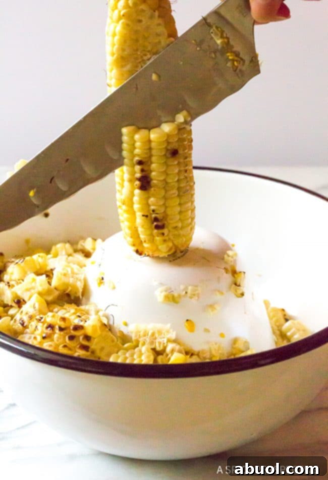 Closeup of a knife removing corn kernels from the cob into a bowl. 