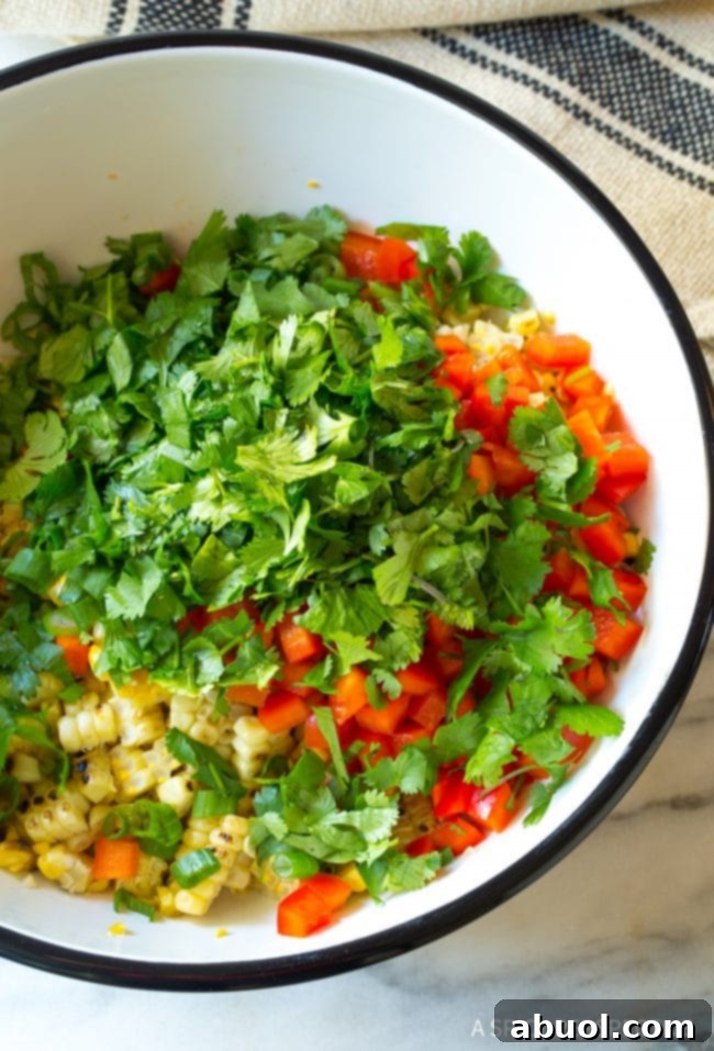 Overhead of a bowl filled with ingredients for street corn salad - cilantro, red bell pepper, corn, green onions. 