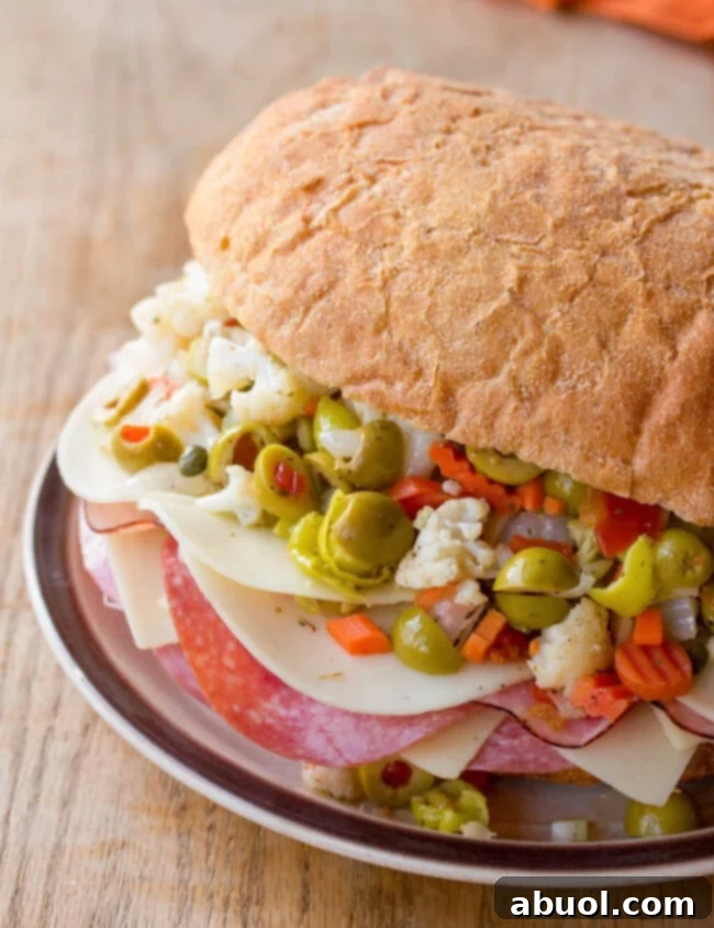 A freshly made New Orleans Muffuletta Sandwich, cut into wedges and served on a rustic plate, showcasing layers of meat, cheese, and a vibrant olive salad.