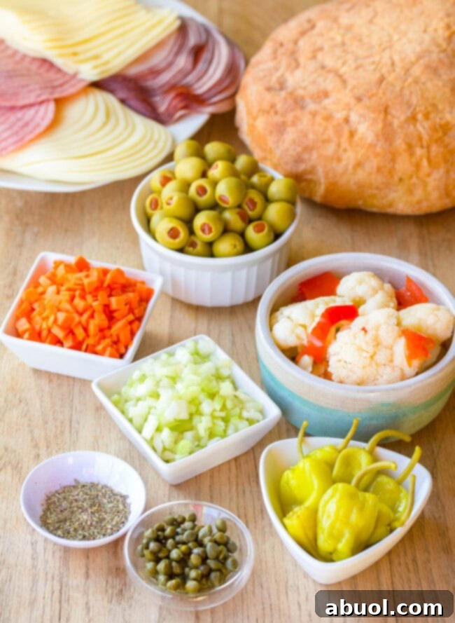 A wooden board displays all the fresh ingredients needed for a Muffuletta sandwich, including olives, giardiniera, deli meats, cheeses, and Italian bread.