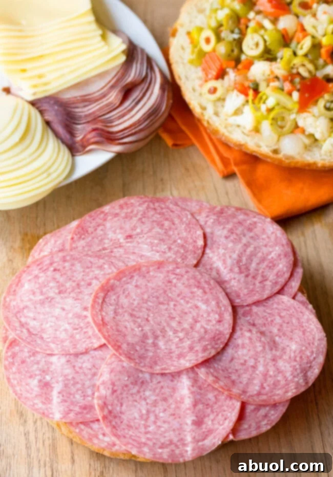 A final layer of nutty Swiss cheese completes the meat and cheese foundation of the Muffuletta, preparing for the star olive salad.