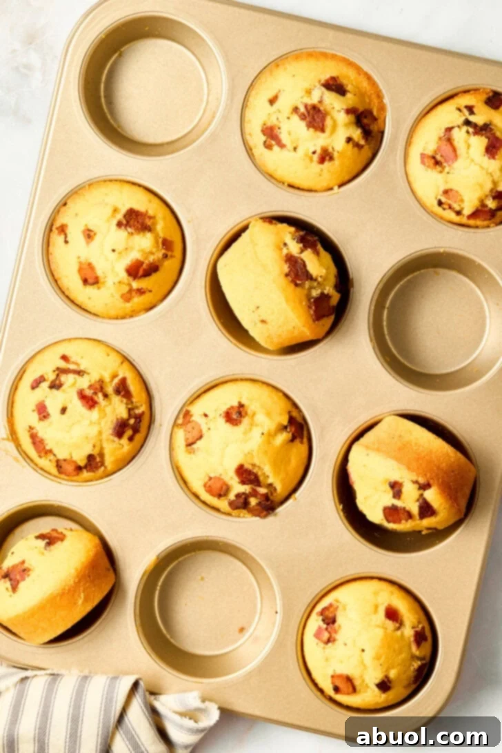 Heavenly Bacon Corn Muffins 2 Warm cornbread muffins in a pan with bacon bits and maple syrup drizzle, showcasing the salty-sweet delight.