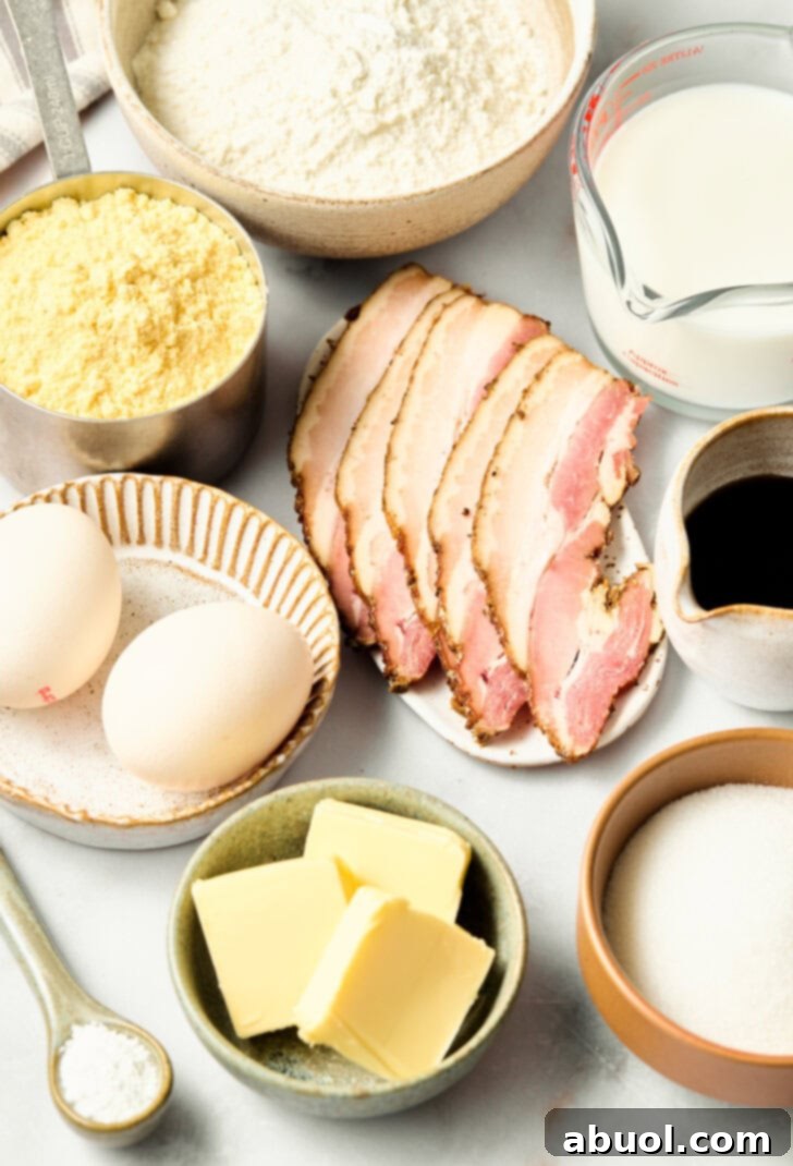 Heavenly Bacon Corn Muffins 5 Ingredients for corn muffins laid out on a kitchen counter, including cornmeal, flour, eggs, milk, bacon, and maple syrup.