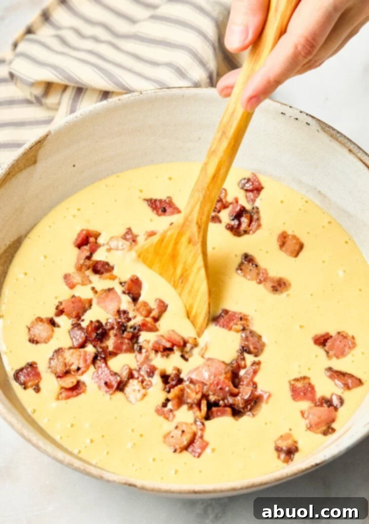 Heavenly Bacon Corn Muffins 7 Chopped cooked bacon being mixed into a golden cornbread batter in a large bowl.
