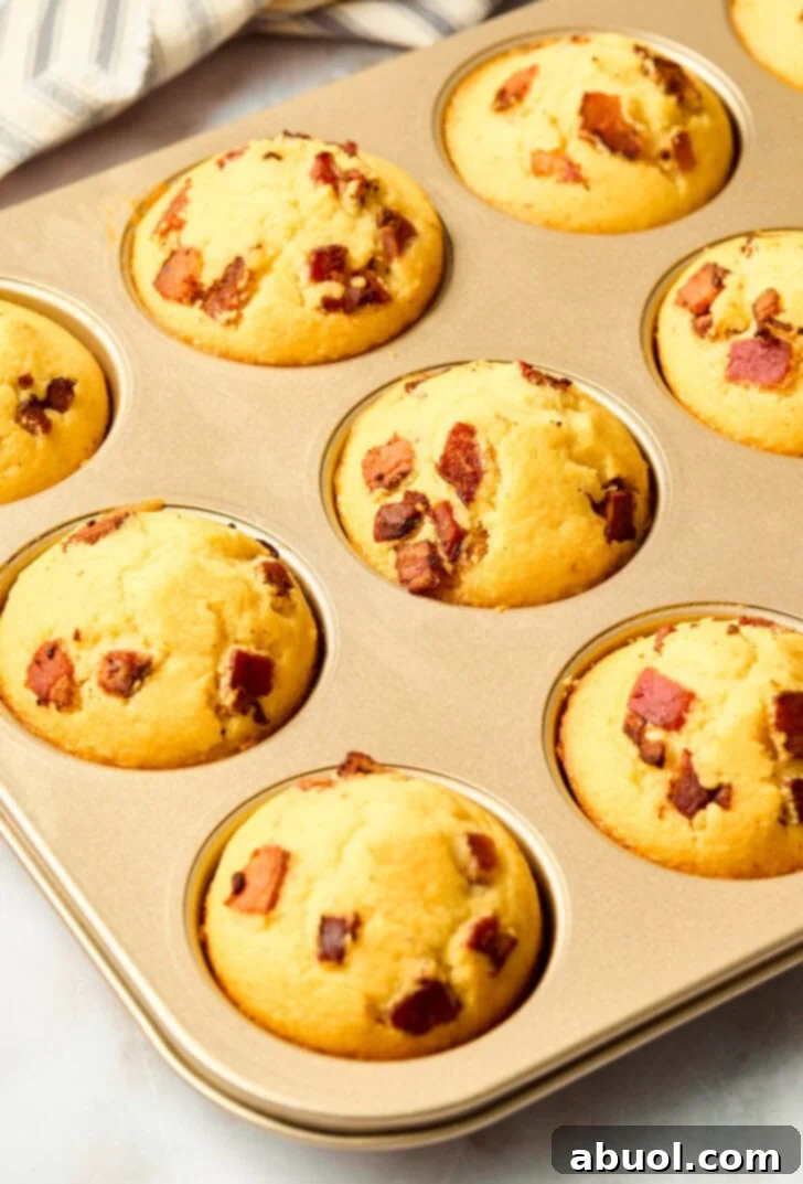 Heavenly Bacon Corn Muffins 9 A batch of golden-brown, freshly baked corn muffins in a muffin pan, straight from the oven.