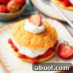 A vibrant, fully assembled Strawberry Shortcake with golden cornmeal biscuit, red berries, and white whipped cream.