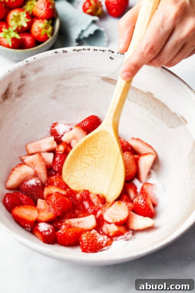 Freshly sliced strawberries gently tossed with granulated sugar in a clear bowl, beginning the maceration process.