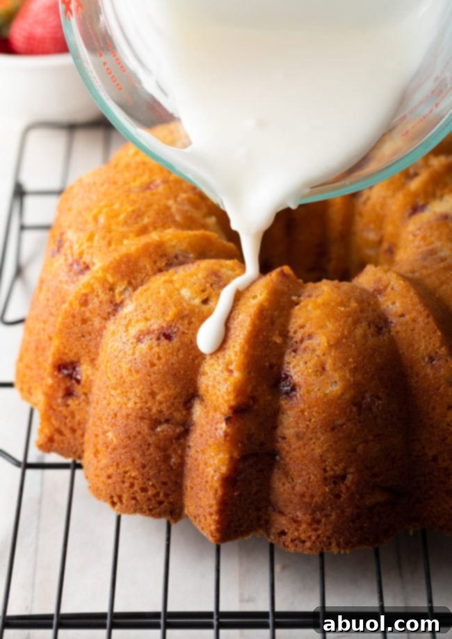 Baked strawberry bundt cake being drizzled with lemon glaze from a glass measuring cup.