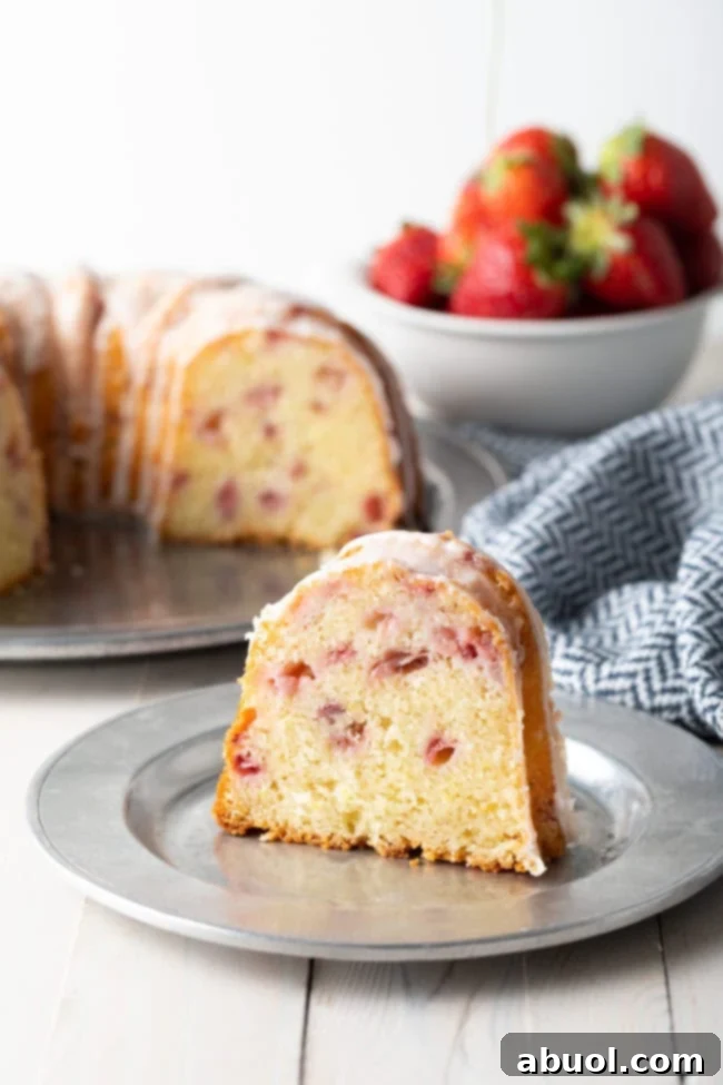 Slice of strawberry bundt cake on a plate with the rest of the cake in the background.