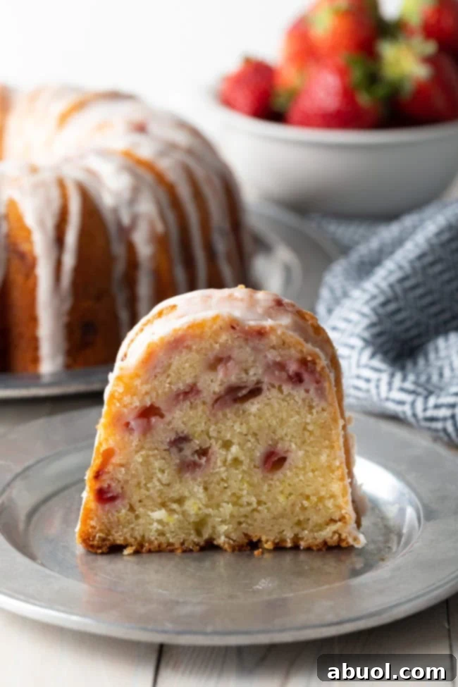 Slice of glazed strawberry cake on a silver plate.