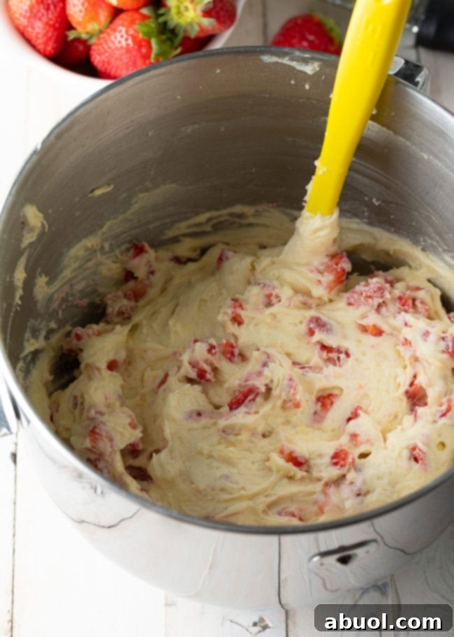 Strawberry cake batter with strawberries added and being stirred with a yellow spatula.