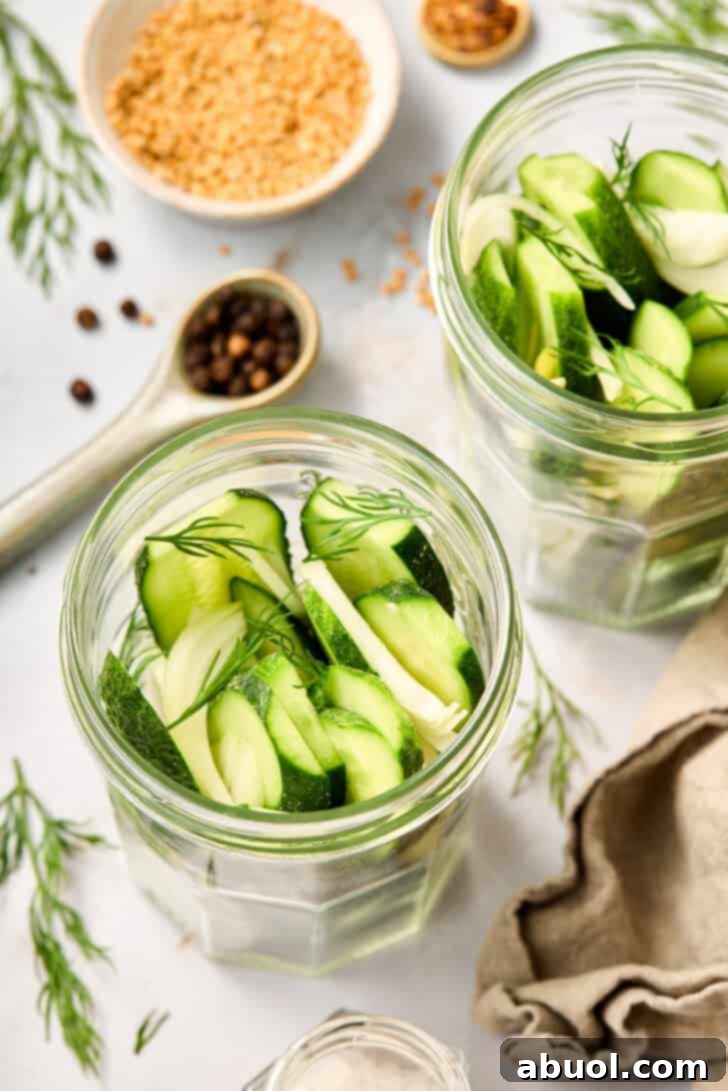 Close-up of a glass jar packed with sliced cucumbers, onions, and fresh dill, awaiting brine