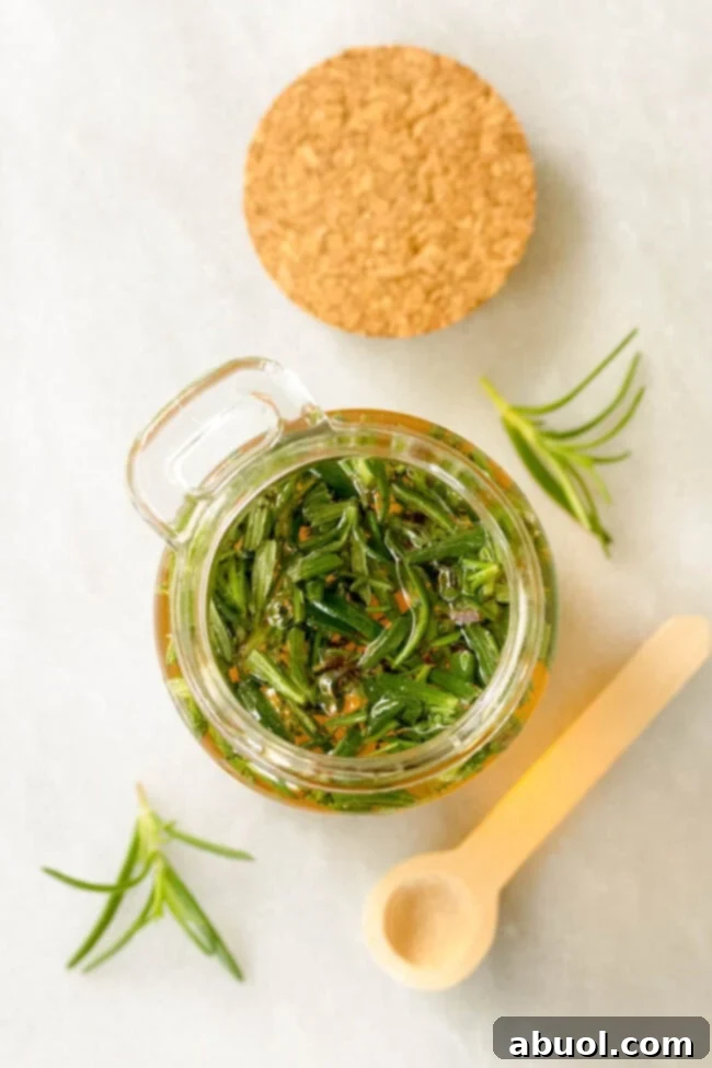 A close-up, overhead shot reveals fresh herbs, specifically rosemary, gracefully steeping in a small jar of golden honey, ready for infusion.
