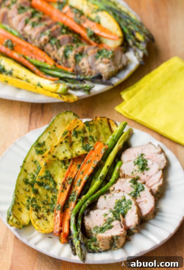 Sliced grilled pork tenderloin with chimichurri and roasted vegetables on a plate, ready to be enjoyed.