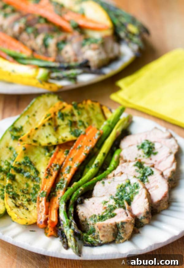 A perfectly plated dish featuring grilled pork tenderloin, generously topped with chimichurri, accompanied by roasted seasonal vegetables.