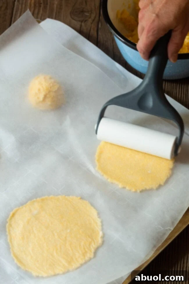 Portioned tortilla dough balls are carefully rolled out into flat, round low-carb tortillas on a parchment-lined baking sheet.