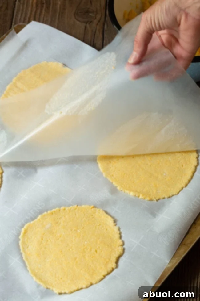 A hand gently peels back a sheet of wax paper to reveal perfectly round, flat low-carb tortillas, ready for baking.