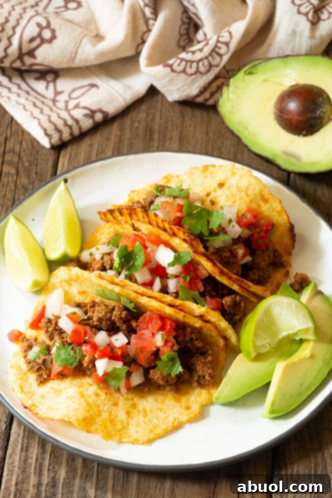 A beautifully arranged plate featuring three fully assembled tacos with low-carb cauliflower tortillas, garnished with fresh lime wedges and sliced avocado.