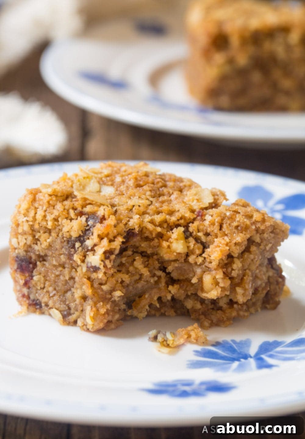 Close-up shot of a single oat breakfast bar on a plate with a bite taken out, revealing its soft, chewy interior with visible dates and nuts.